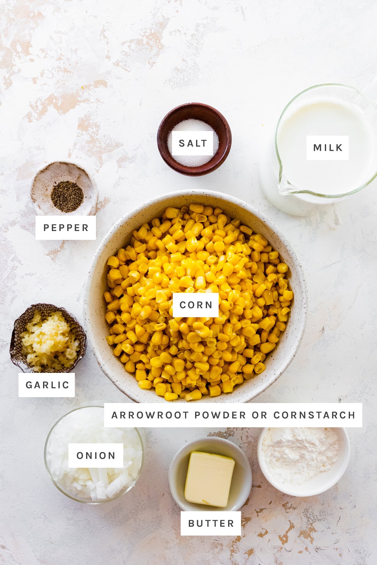 Ingredients measured out to make Creamed Corn: pepper, salt, milk, corn, garlic, onion, butter and arrowroot powder.