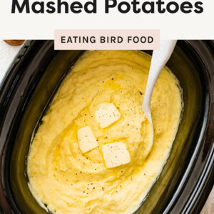 Slow Cooker Mashed Potatoes in a slow cooker with a spoon and topped with butter pads.