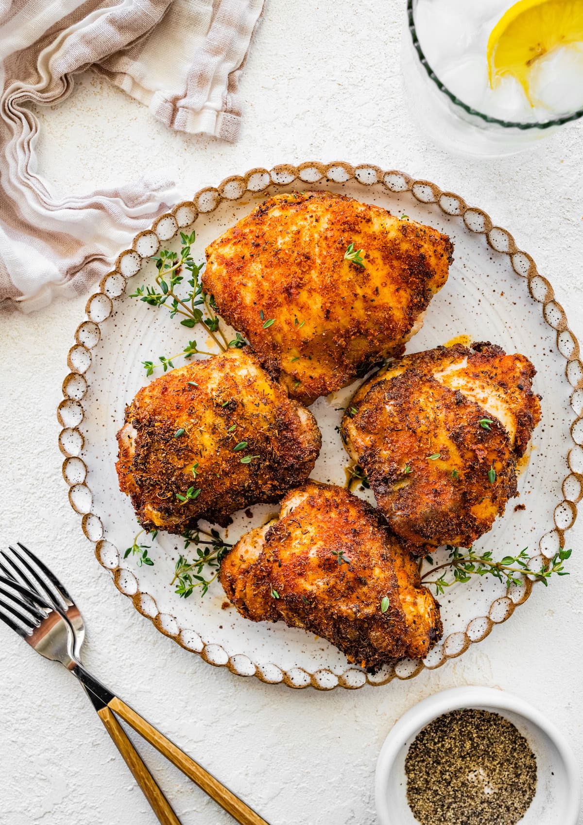 Four bone-in chicken thighs served on a white dinner plate topped with fresh parsley and thyme.