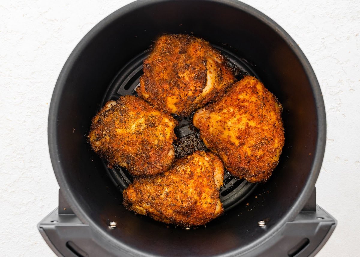 Four bone-in chicken thighs cooked in the basket of an air fryer.