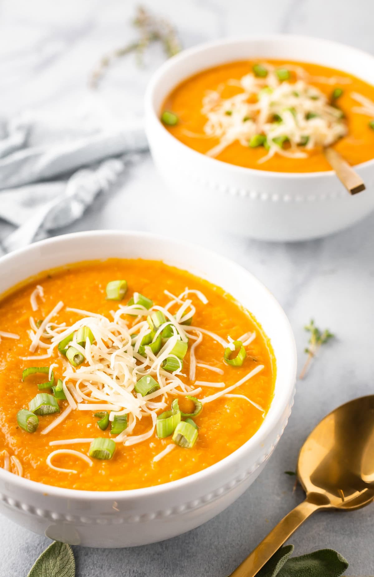 Two bowls of carrot parsnip soup garnished with scallions and shredded gruyere cheese.