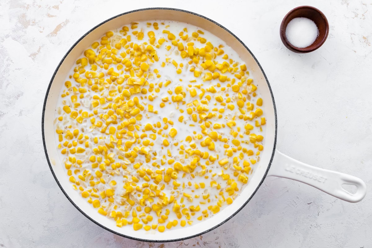 The milk arrowroot powder mixture poured over corn in a white skillet for the creamed corn.