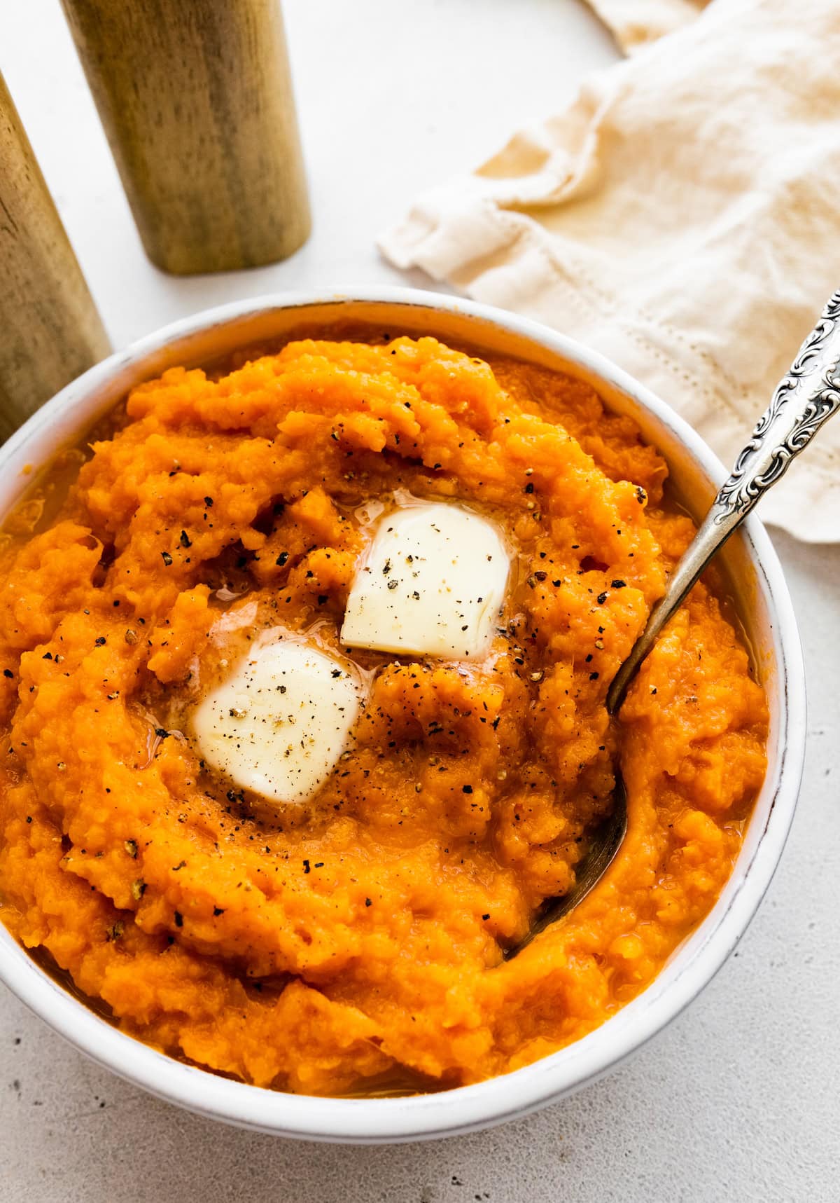 Mashed sweet potato in a bowl topped with two slices of butter and seasonings.