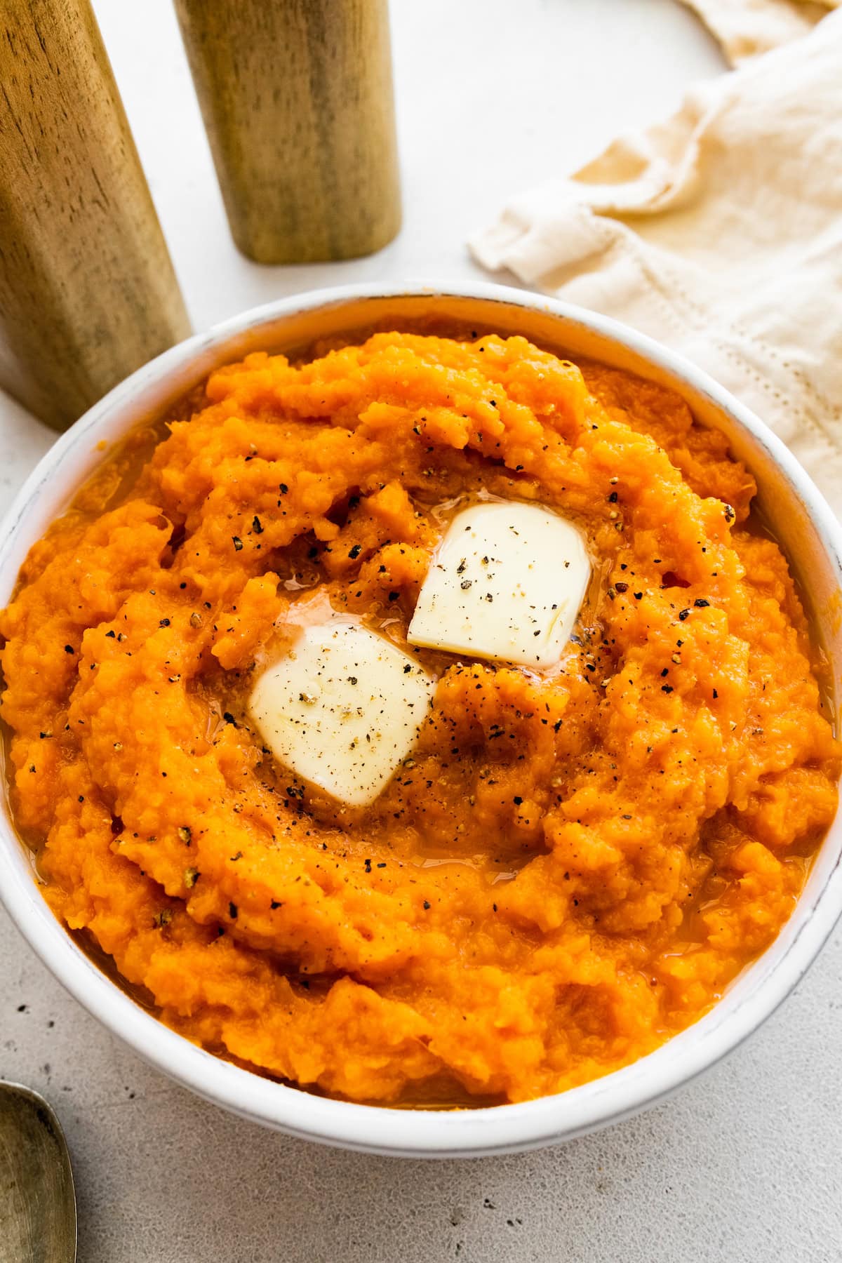 Mashed sweet potato in a bowl topped with two slices of butter and seasonings.
