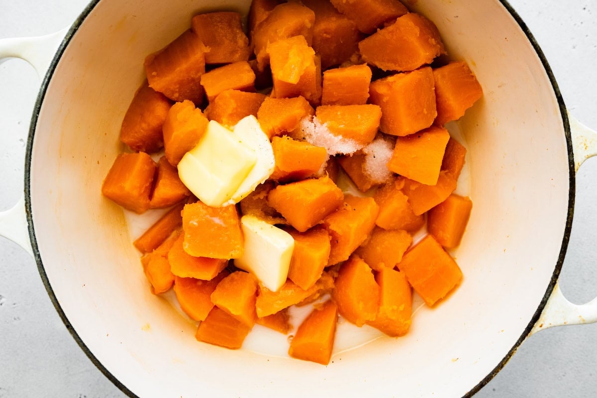 Cooked sweet potato chunks in a large pot with slices of butter.