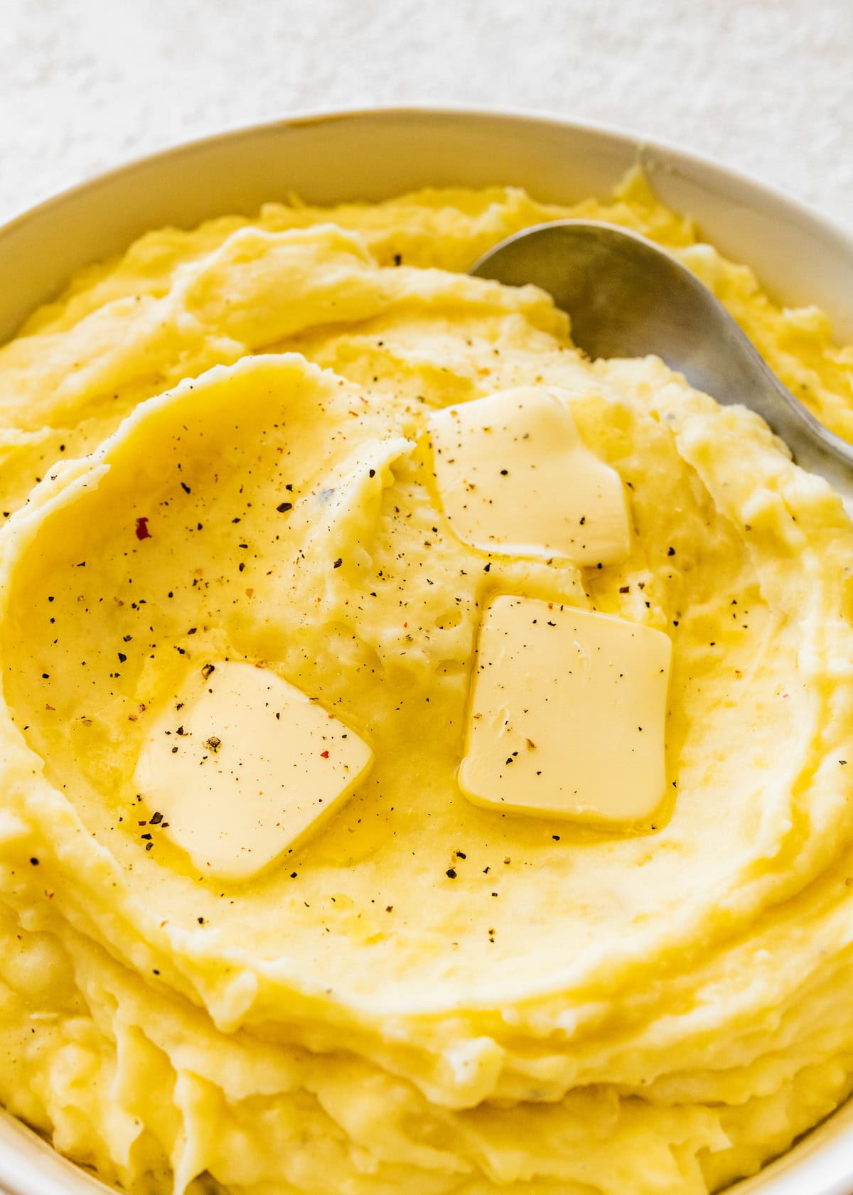Slow cooker mashed potatoes in a bowl topped with three slices of butter and cracked pepper.