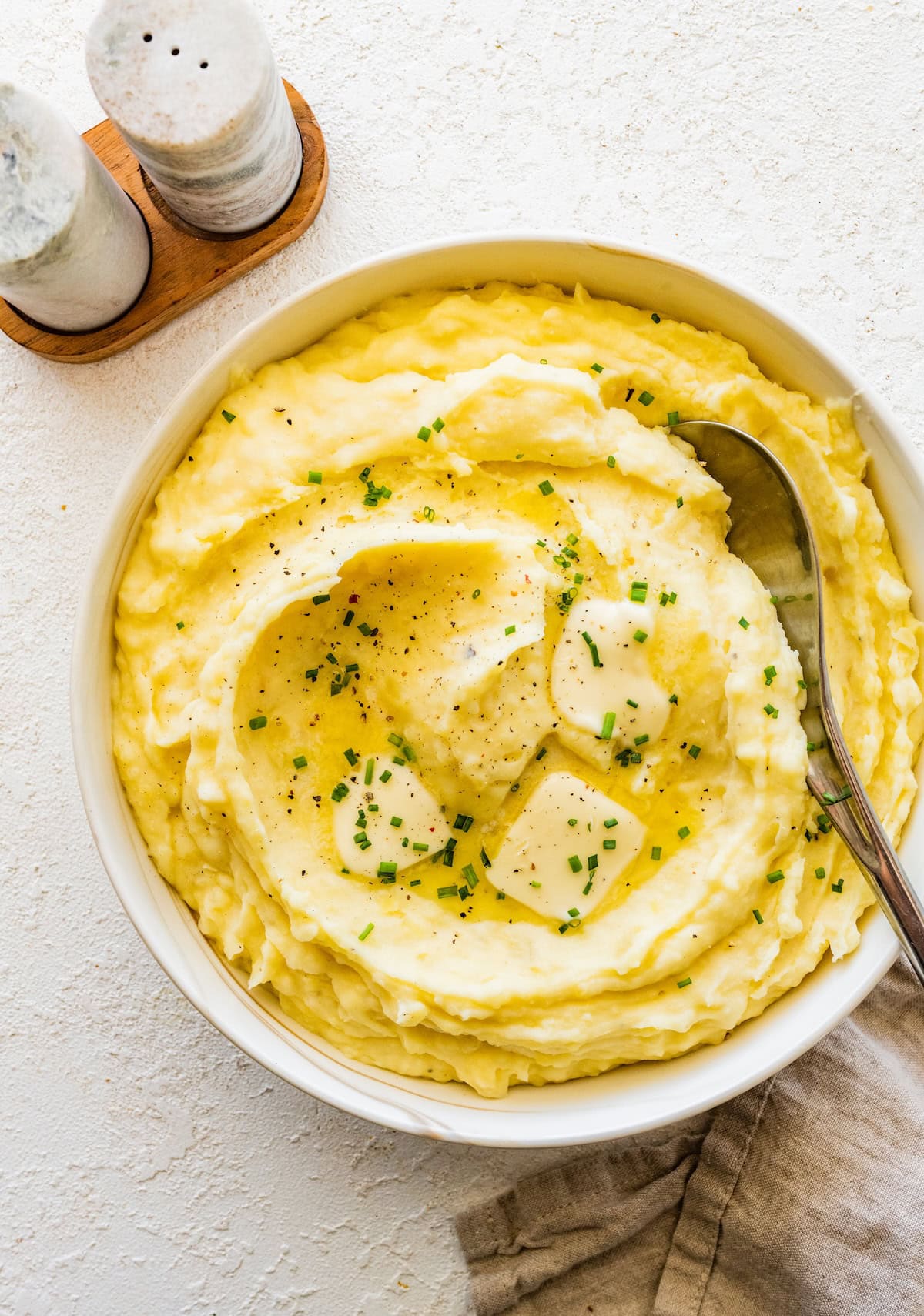Slow cooker mashed potatoes in a bowl, topped with pepper, sliced butter, and fresh chives.