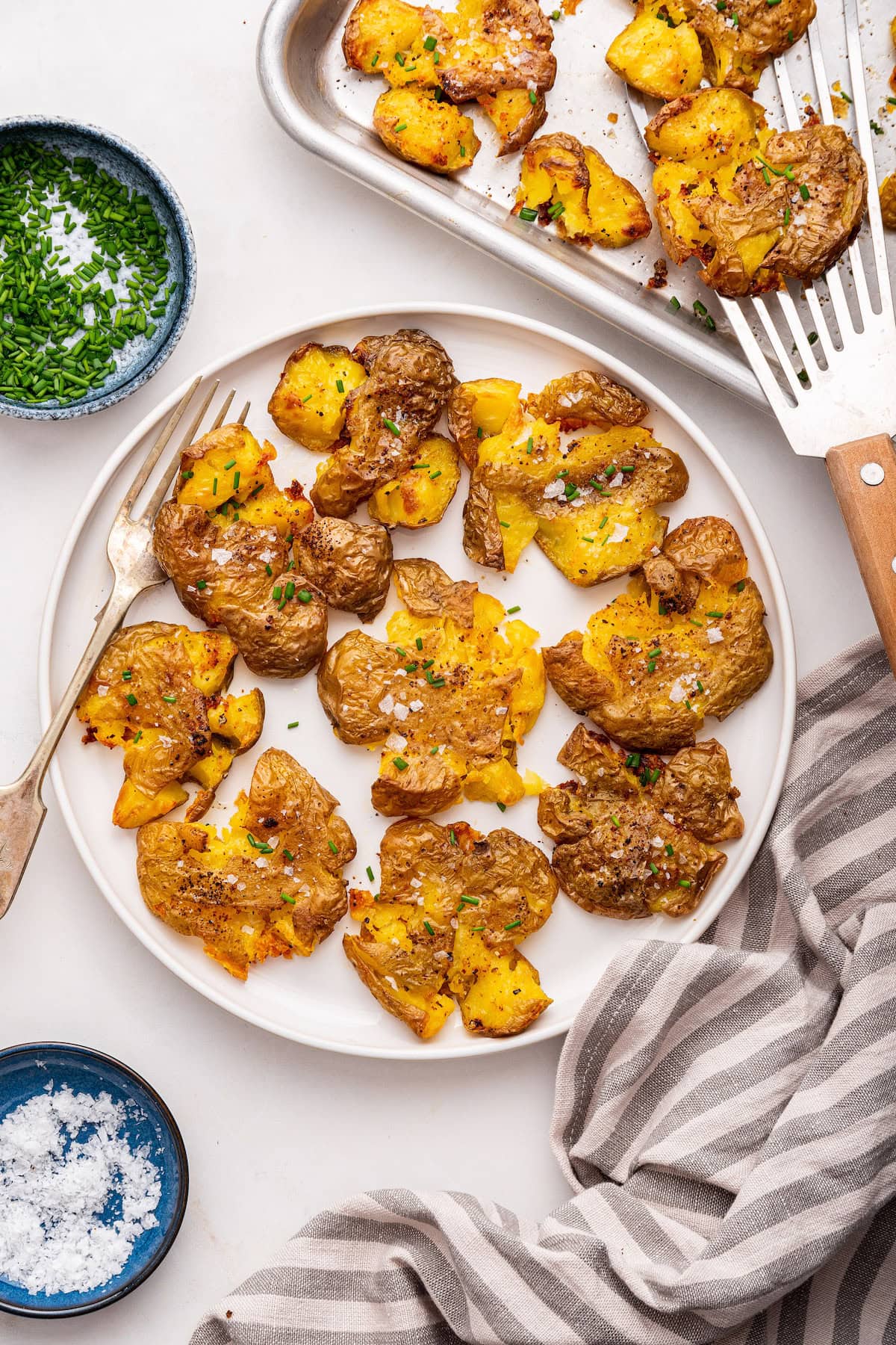 Smashed potatoes garnished with fresh chives and salt on a plate.