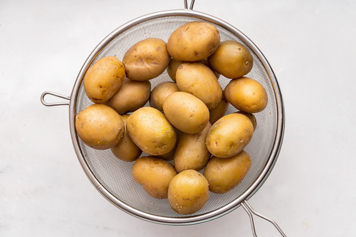 Multiple potatoes in a metal strainer.