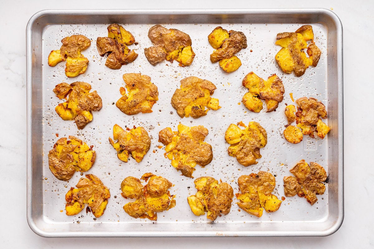 Seasoned smashed potatoes on a baking tray.