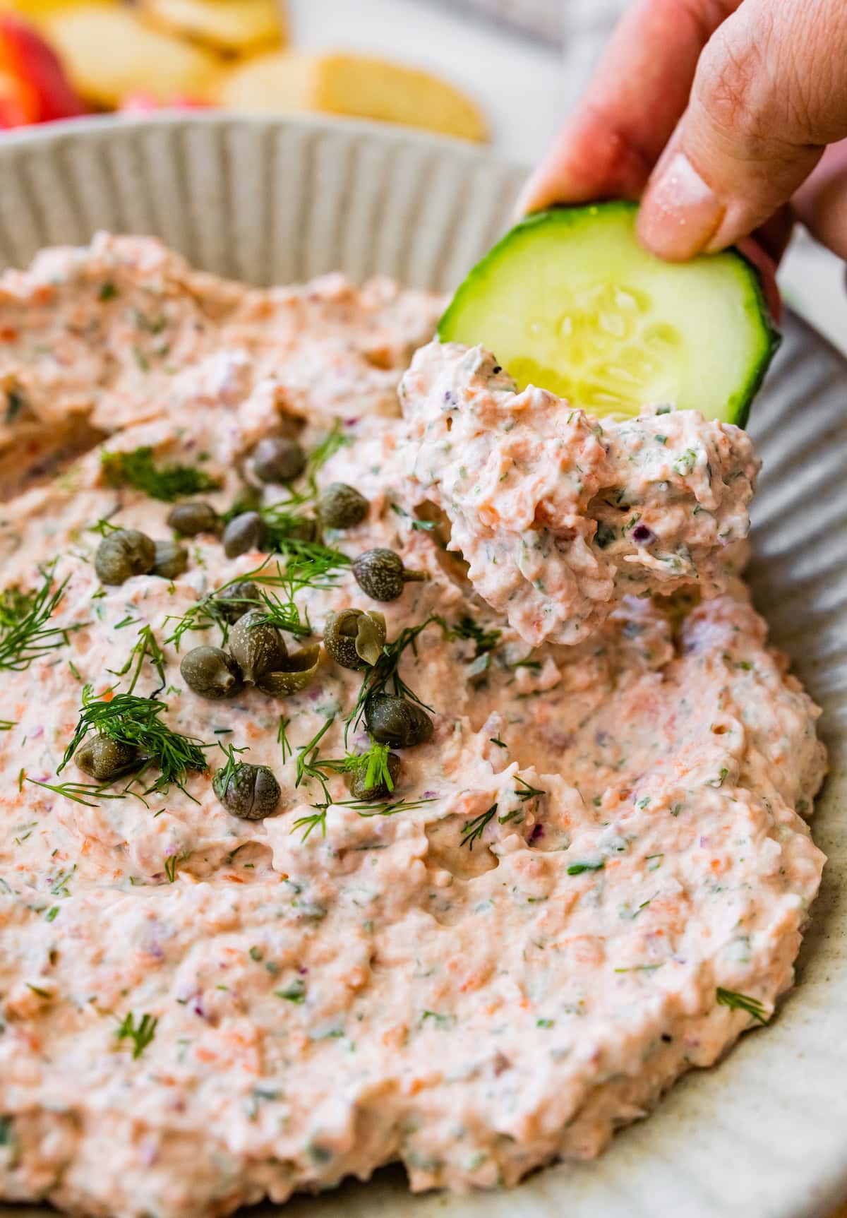 A woman's hand dips a sliced cucumber in a smoked salmon dip.