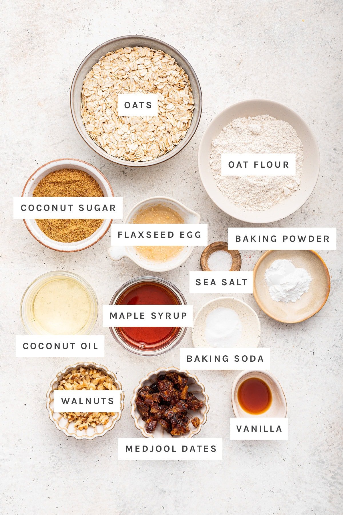 Ingredients measured out to make Oatmeal Date Cookies: oats, oat flour, coconut sugar, flaxseed egg, baking powder, sea salt, maple syrup, coconut oil, baking soda, walnuts, medjool dates and vanilla.