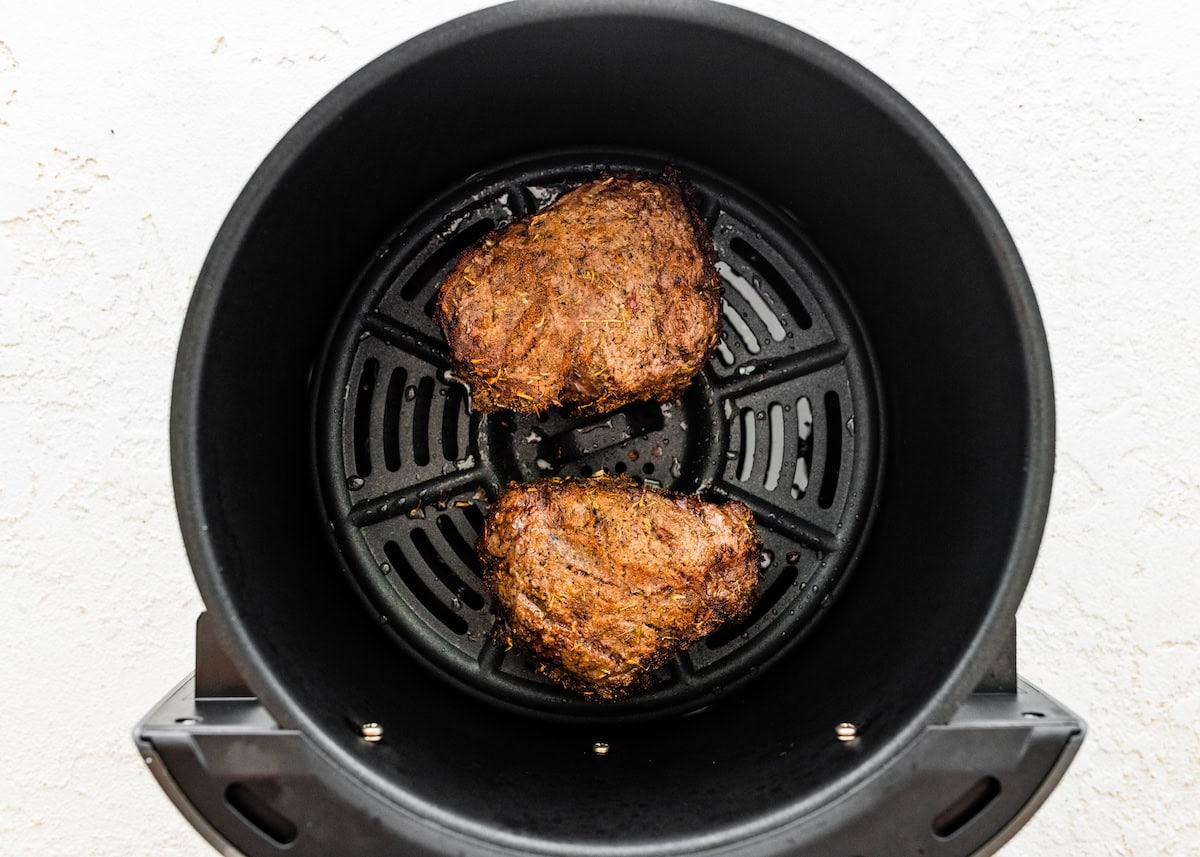 Two cooked filet mignon pieces in the basket of an air fryer.