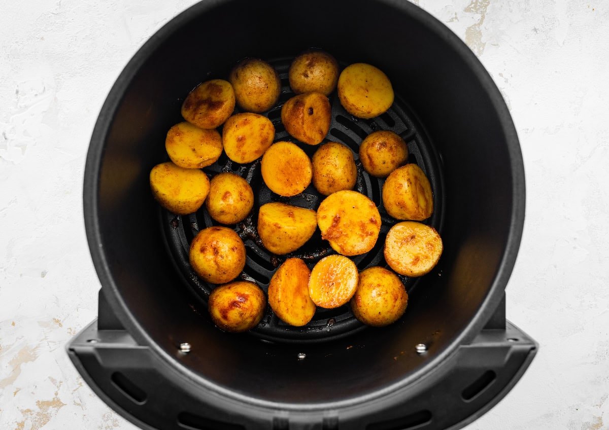 Seasoned potato chunks in an air fryer before being cooked.