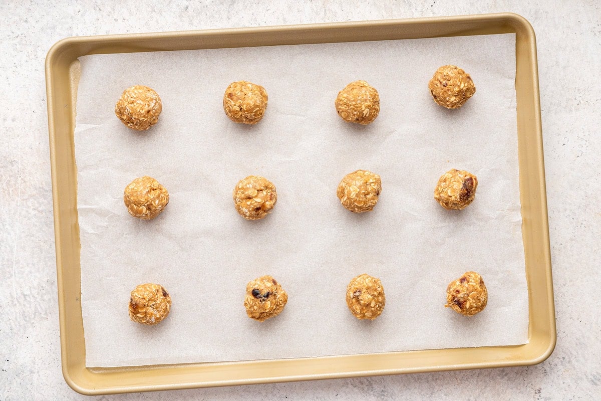 12 oatmeal date cookies dough balls lined up on a parchment-lined baking sheet.
