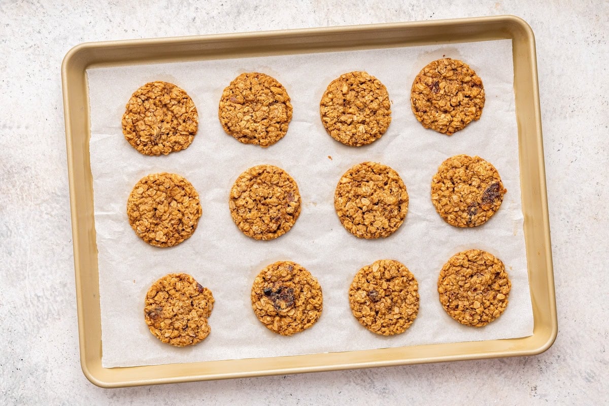 12 baked oatmeal date cookies on a parchment-lined baking sheet.