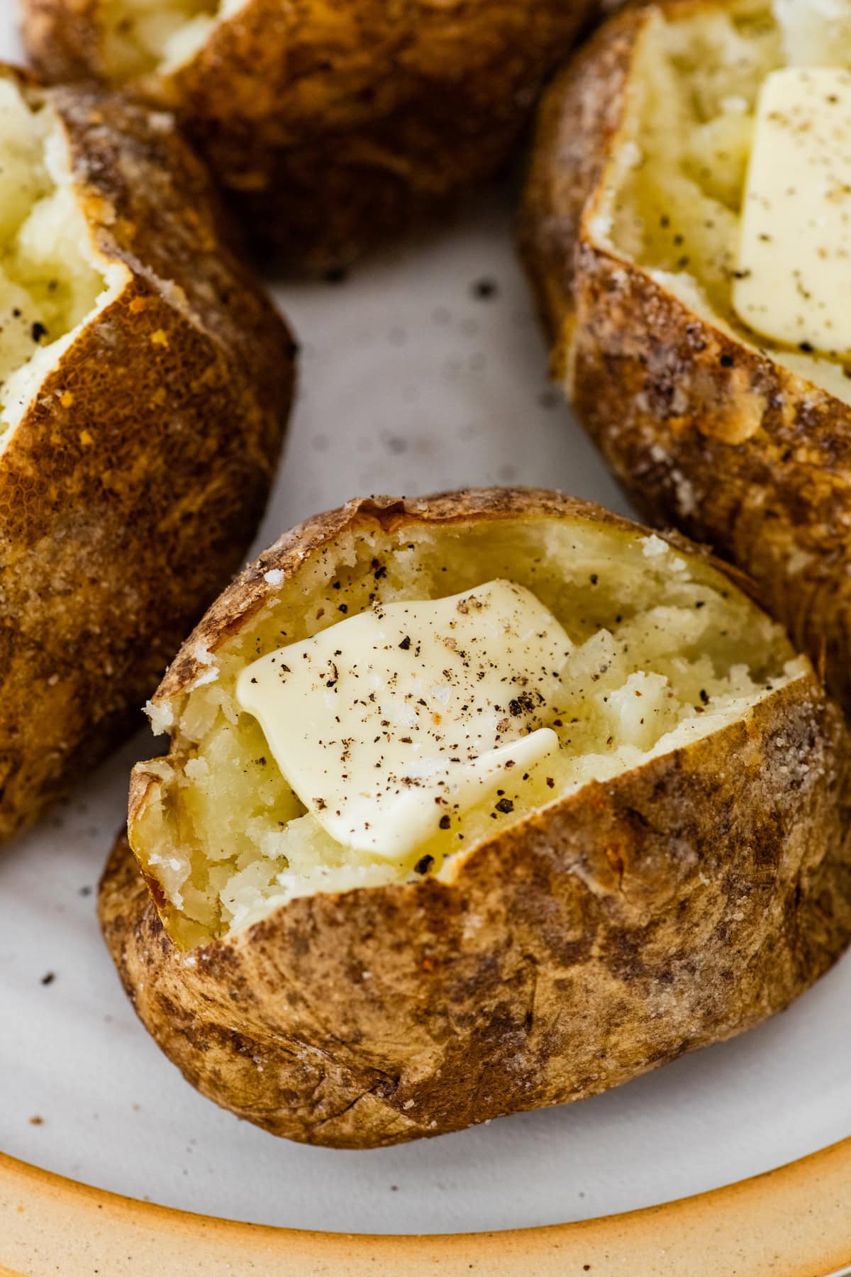 Split open baked potatoes on a plate with seasonings and butter.
