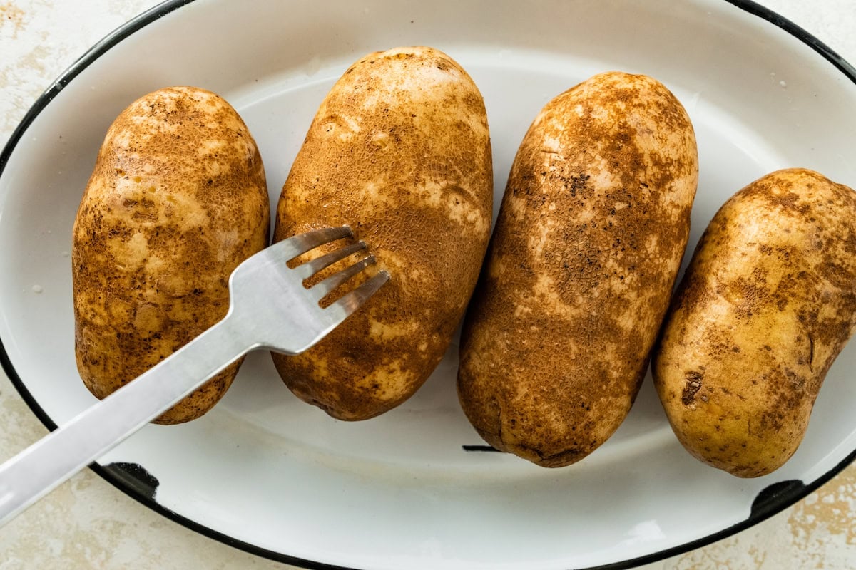 Four potatoes in a pot with a fork poking holes in to the potatoes.