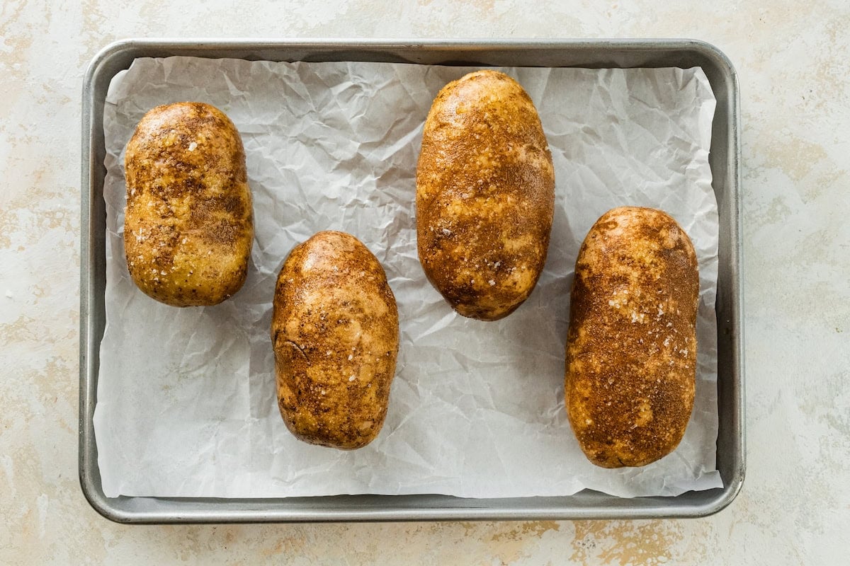 Four potatoes on a baking tray.