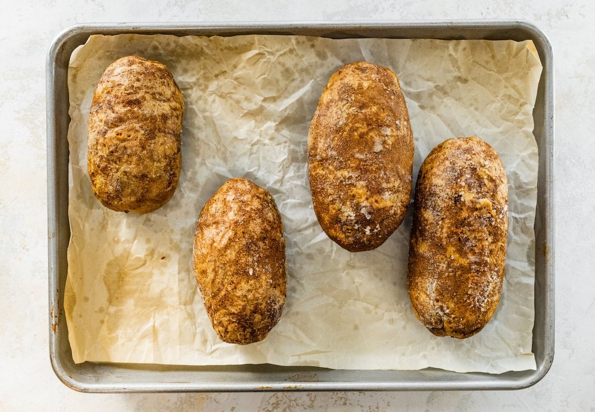 Four potatoes on a baking tray after being baked.