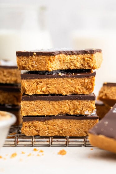 Four peanut butter bars stacked on top of each other on a wire cooling rack. The top bar has a bite taken out of it.