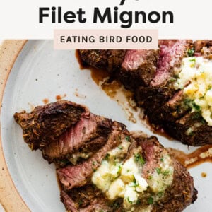 Two Air Fryer Filet Mignons on a plate, sliced and topped with herb butter.