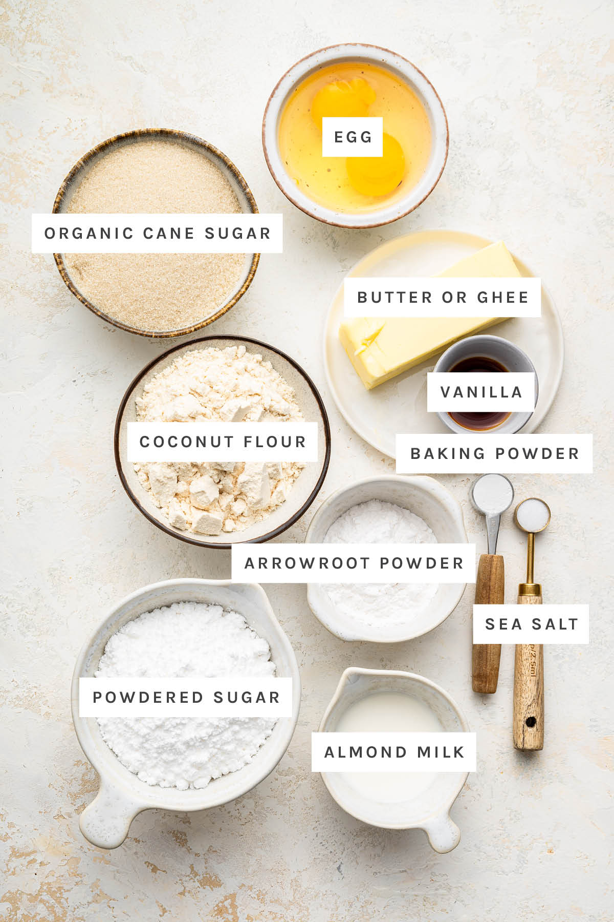 Ingredients measured out to make Gluten Free Sugar Cookies: organic cane sugar, egg, butter, vanilla, coconut flour, baking powder, arrowroot powder, sea salt, powdered sugar and almond milk.