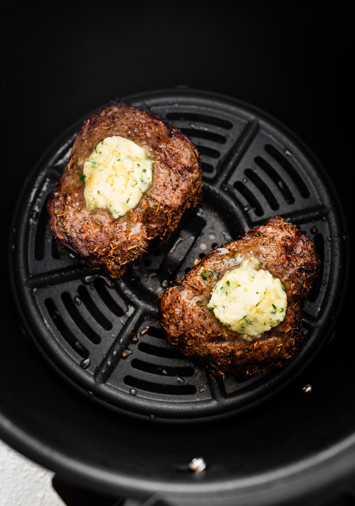 Two filet mignon pieces in an air fryer basket topped with garlic butter.