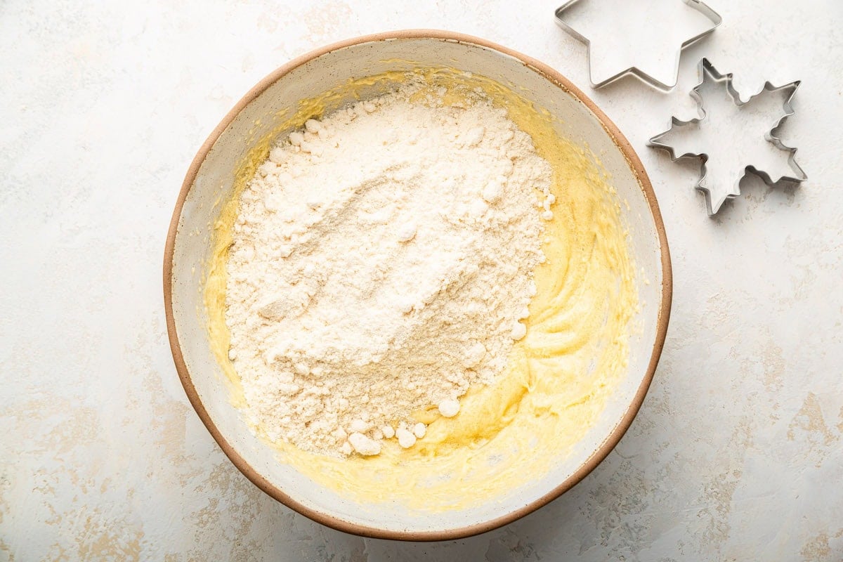 Flour added to a bowl of wet ingredients used in gluten free sugar cookies.
