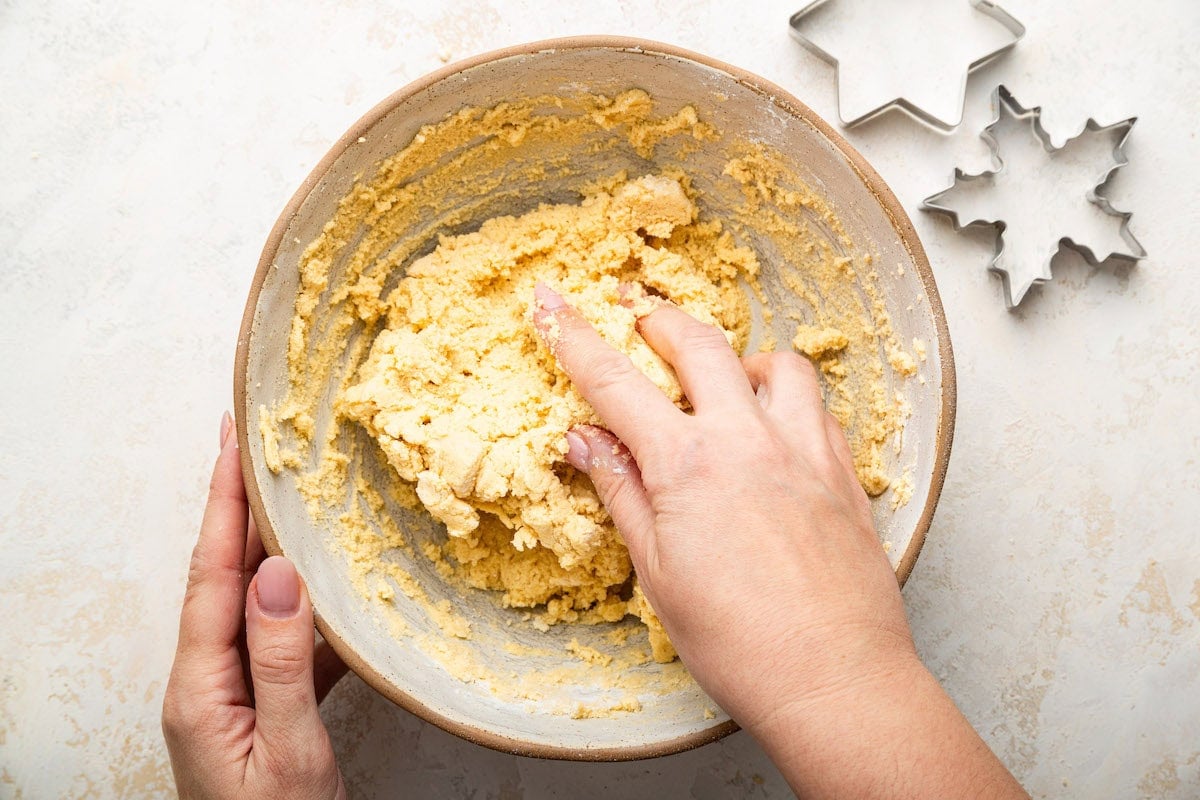 A woman's hand kneads the gluten free sugar cookie dough in a bowl.