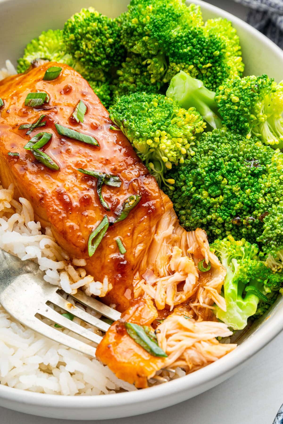 A honey glazed salmon filet in a bowl alongside white rice and broccoli.