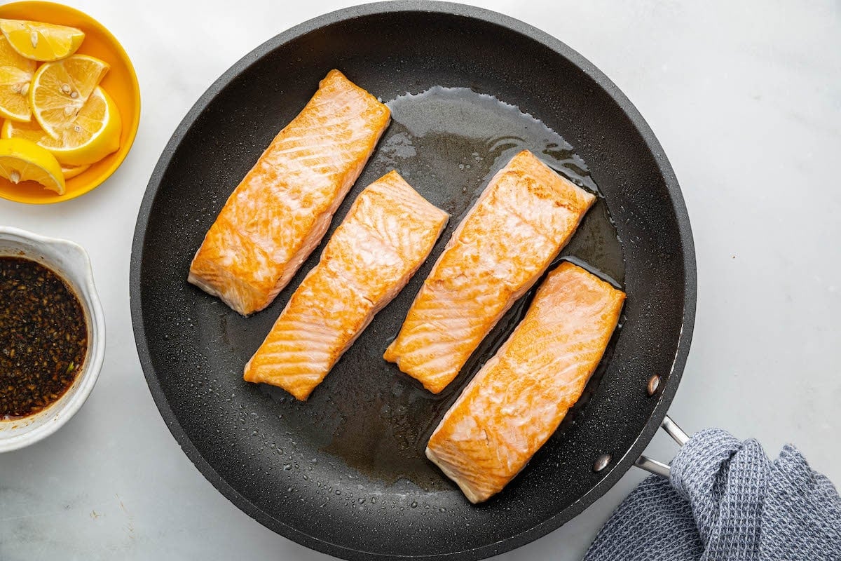 Four salmon filets in cooking in a skillet with olive oil.