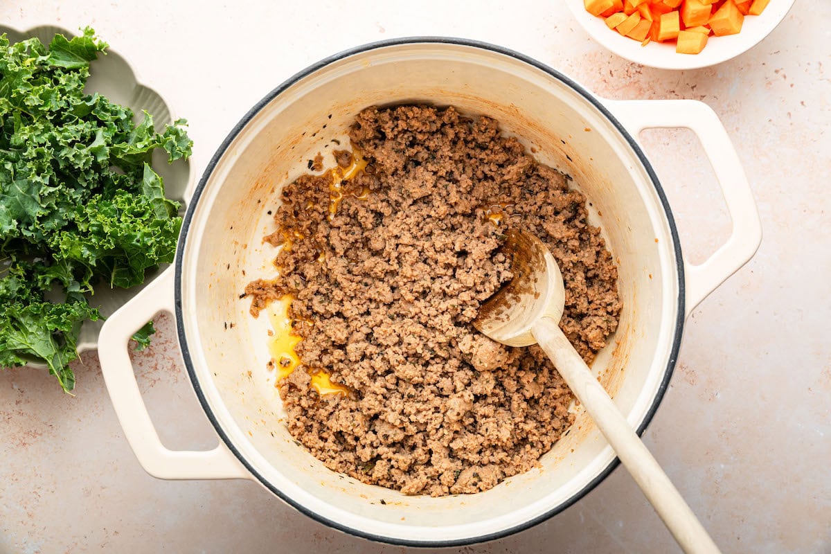 Cooked ground Italian sausage in a dutch oven pot with a wooden spoon.