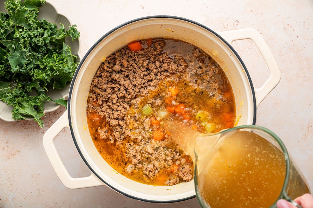 Broth being added to the pot with the sausage and kale soup.