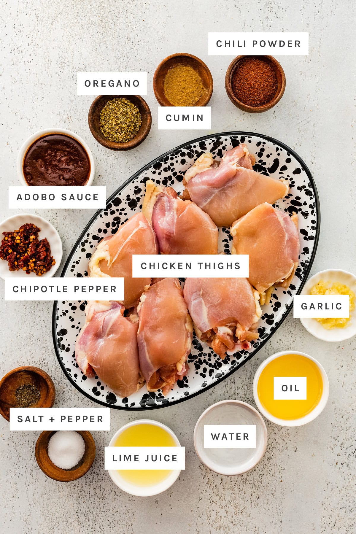 Ingredients measured out to make Chipotle Chicken: chili powder, cumin, oregano, adobo sauce, chipotle pepper, chicken thighs, garlic, oil, water, lime juice, salt and pepper.