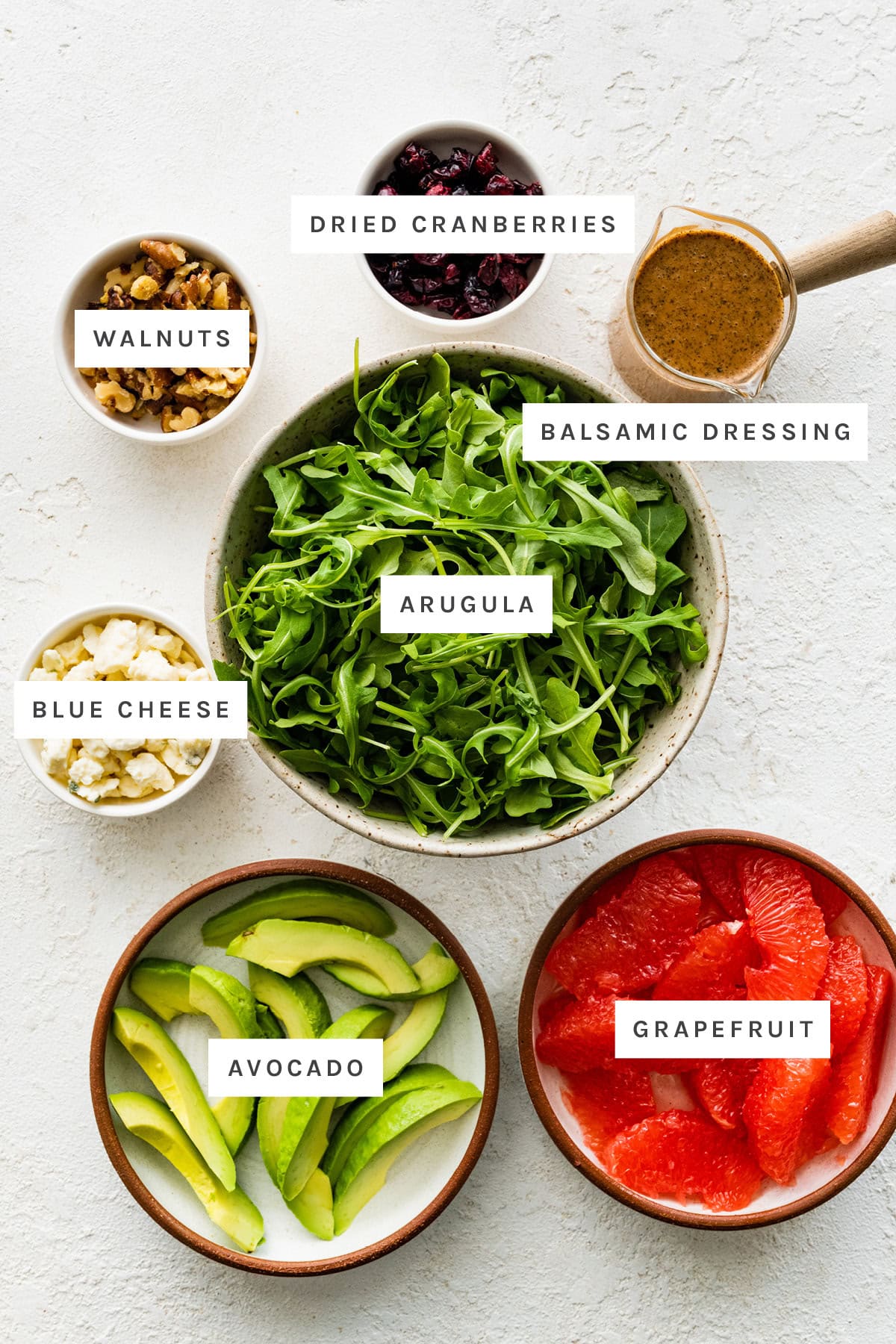 Ingredients measured out to make Avocado Grapefruit Salad: walnuts, dried cranberries, balsamic dressing, arugula, blue cheese, avocado and grapefruit.