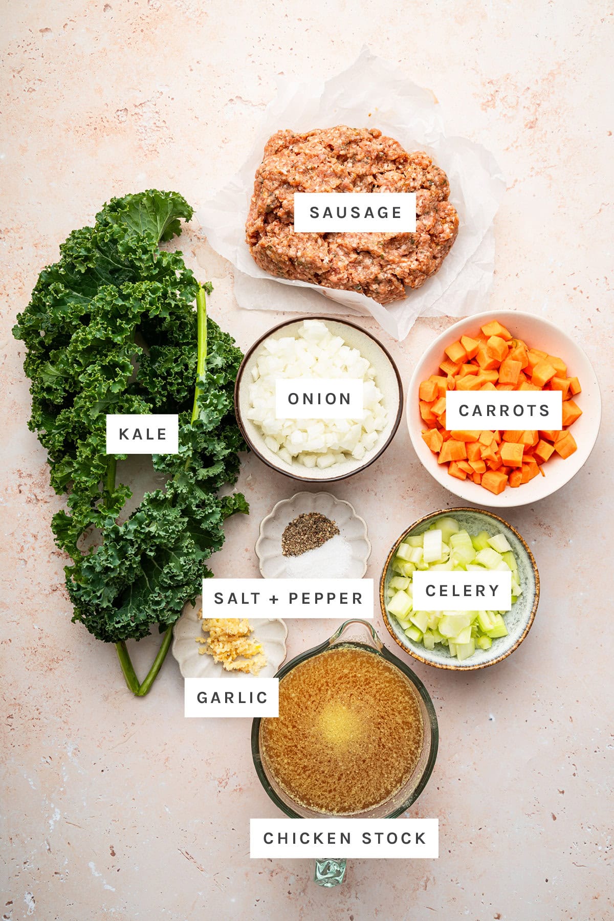 Ingredients measured out to make Sausage Kale Soup: kale, sausage, onion, carrots, salt, pepper, celery, garlic and chicken stock.