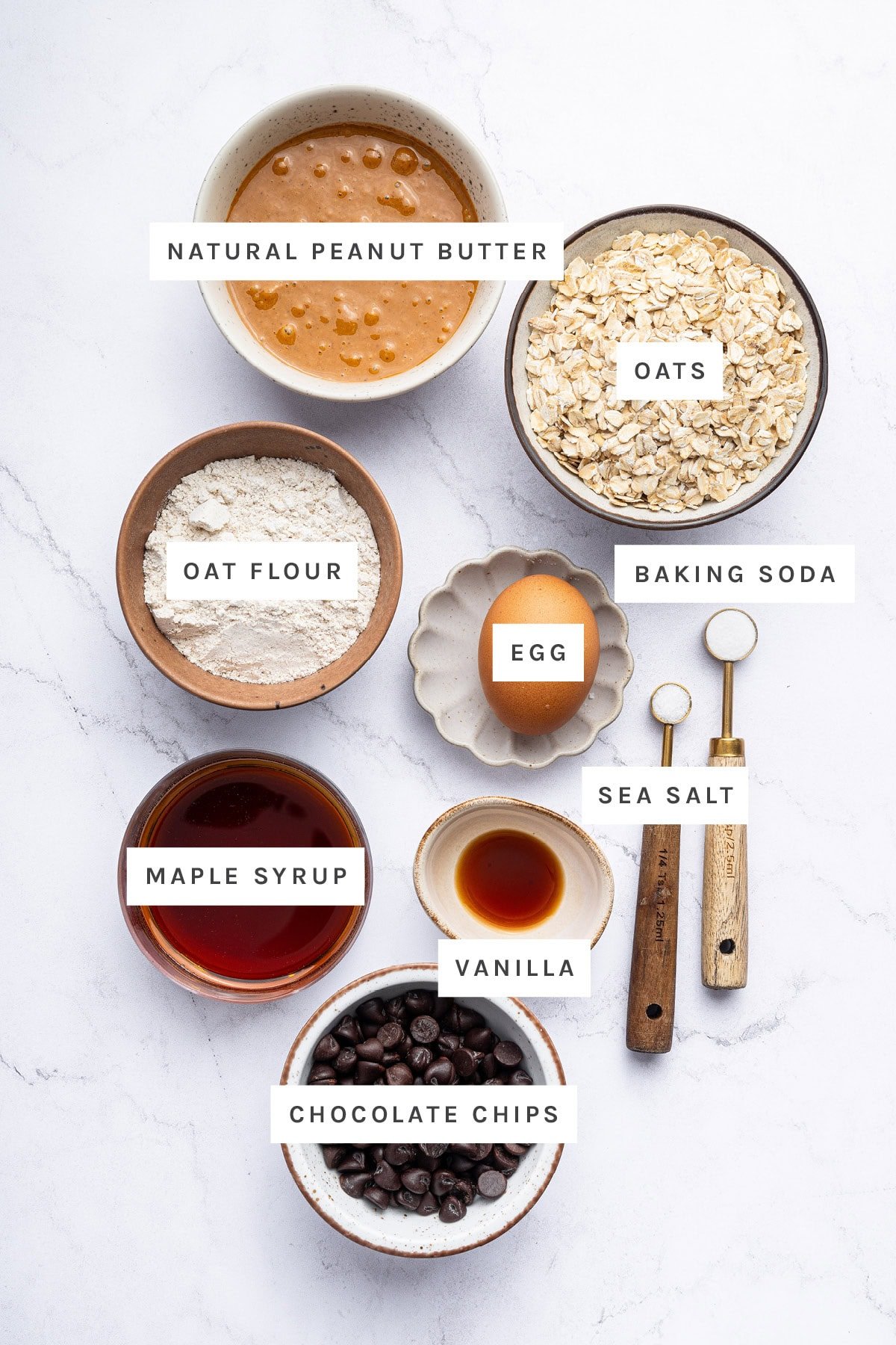 Ingredients measured out to make Peanut Butter Oatmeal Cookies: natural peanut butter, oats, oat flour, egg, baking soda, sea salt, maple syrup, vanilla and chocolate chips.