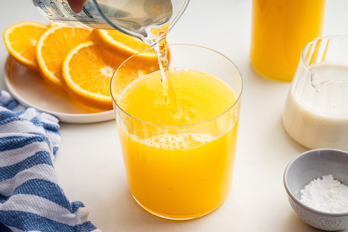 Coconut water being added to a glass with orange juice in it.
