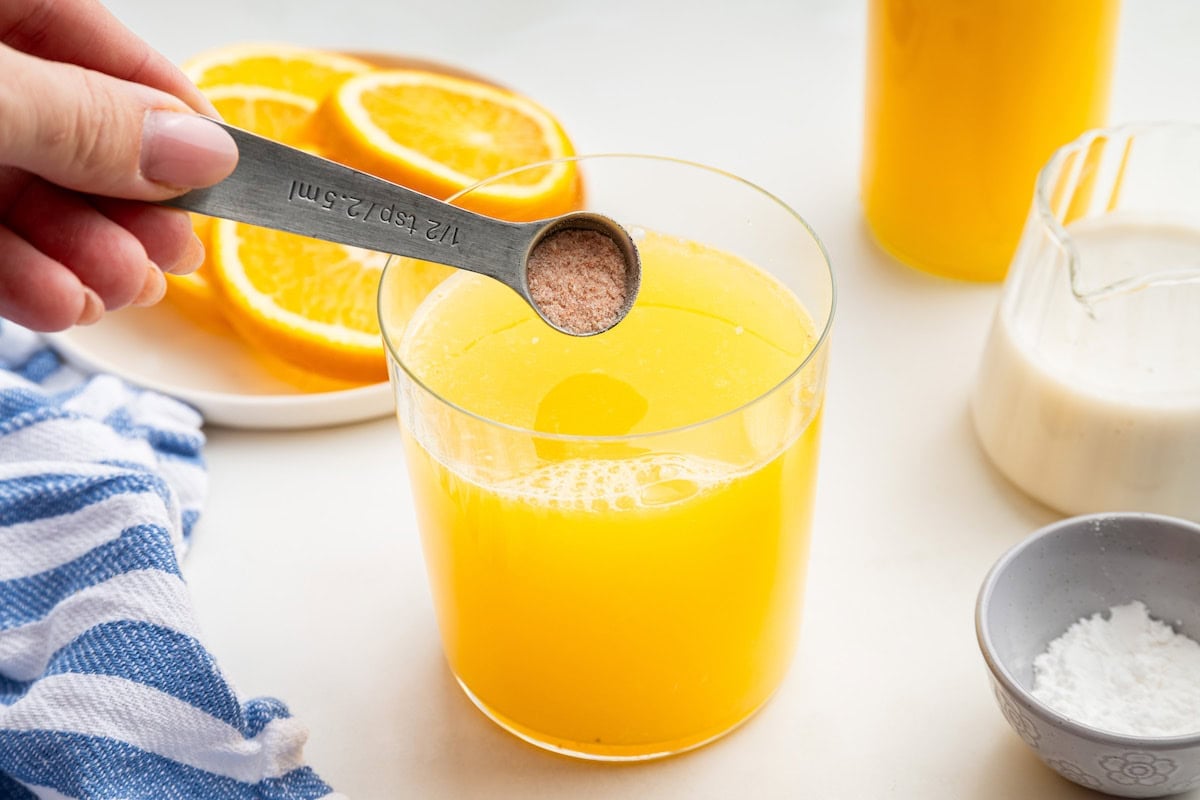Salt being added to a glass with orange juice and coconut water.
