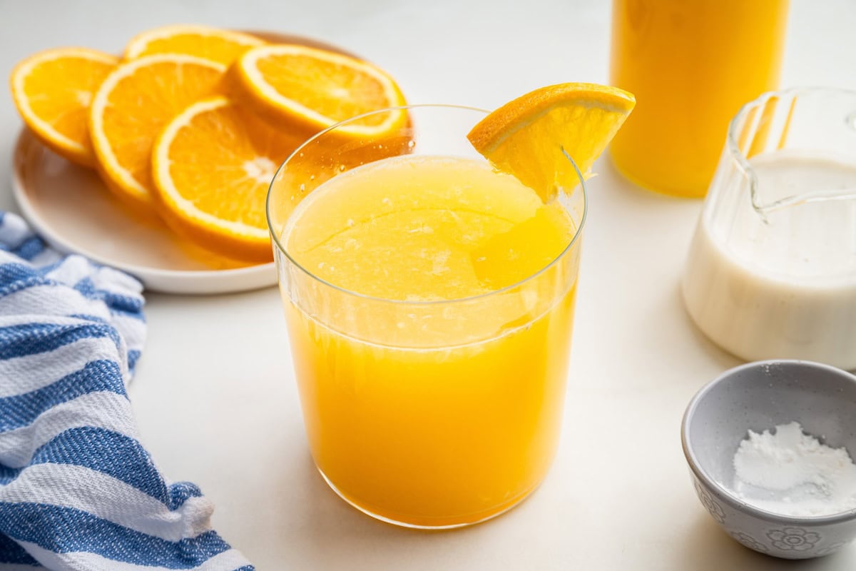 An adrenal cocktail being served in a glass with an orange slice on the rim. A plate of orange slices is in the background.