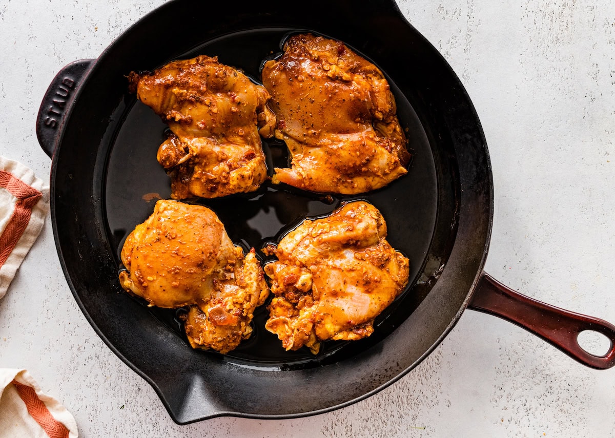 Four chicken thighs cooking in a cast iron skillet.