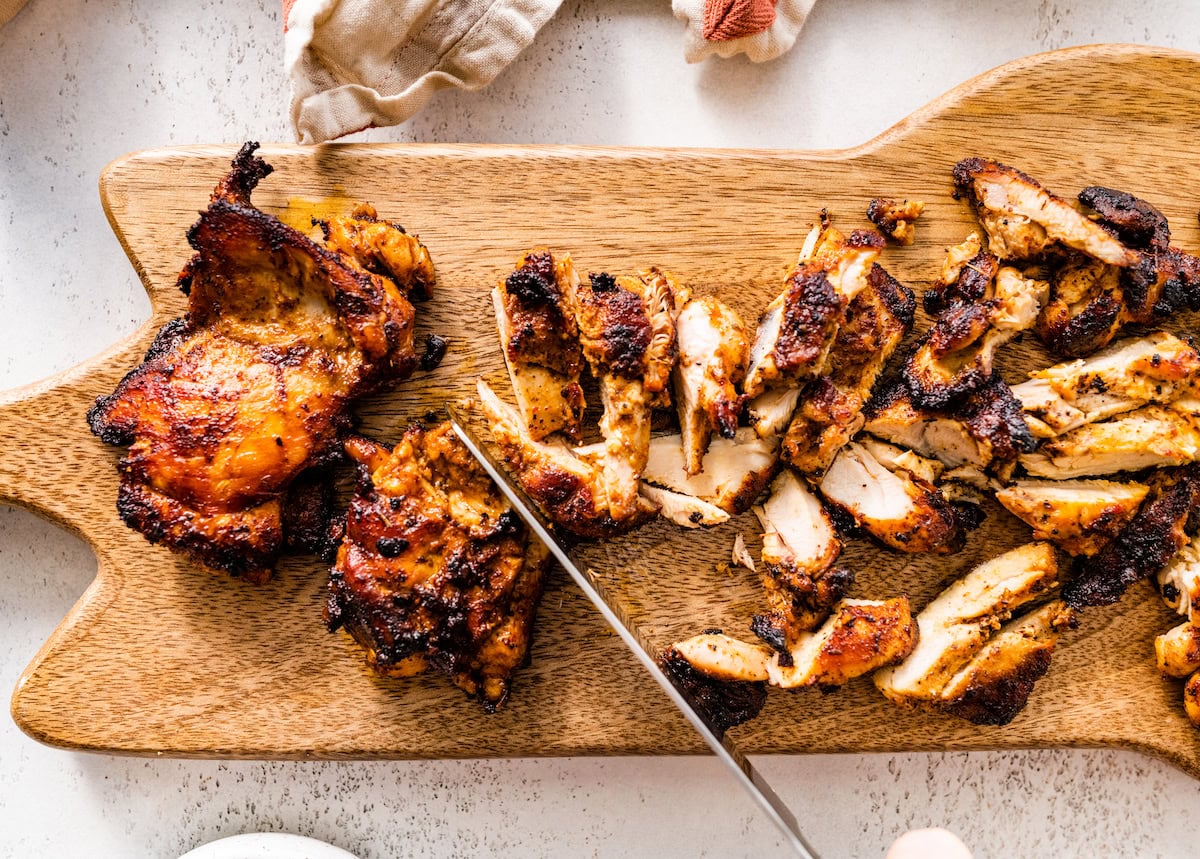 Chipotle chicken being cut with a knife on a wooden cutting board.