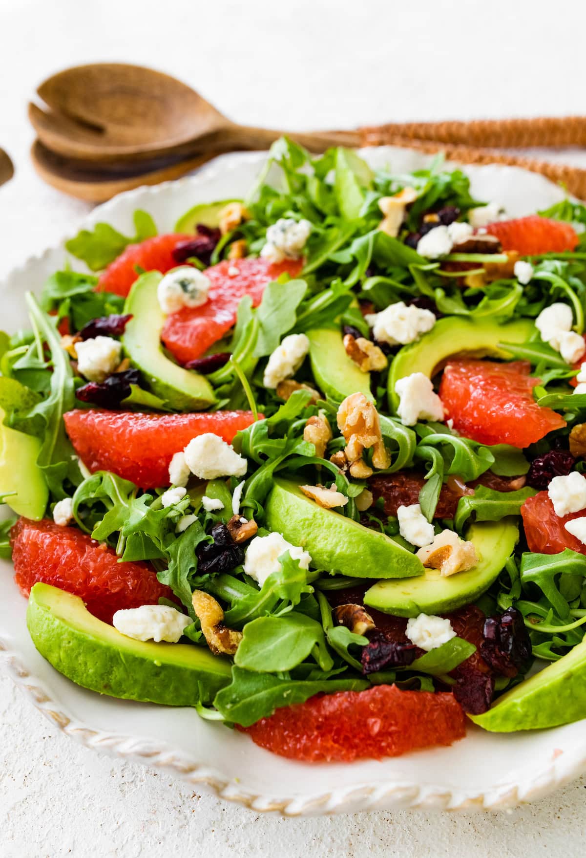 A salad with arugula, avocado, blue cheese, grapefruit, nuts, and cranberries on a white plate.