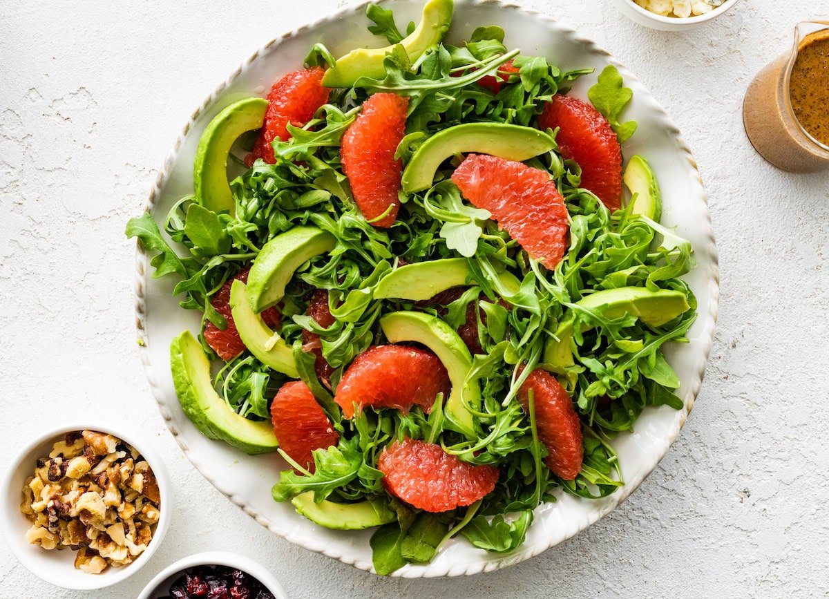 A large white plate with fresh arugula, segments of grapefruit, sliced and sliced avocado.