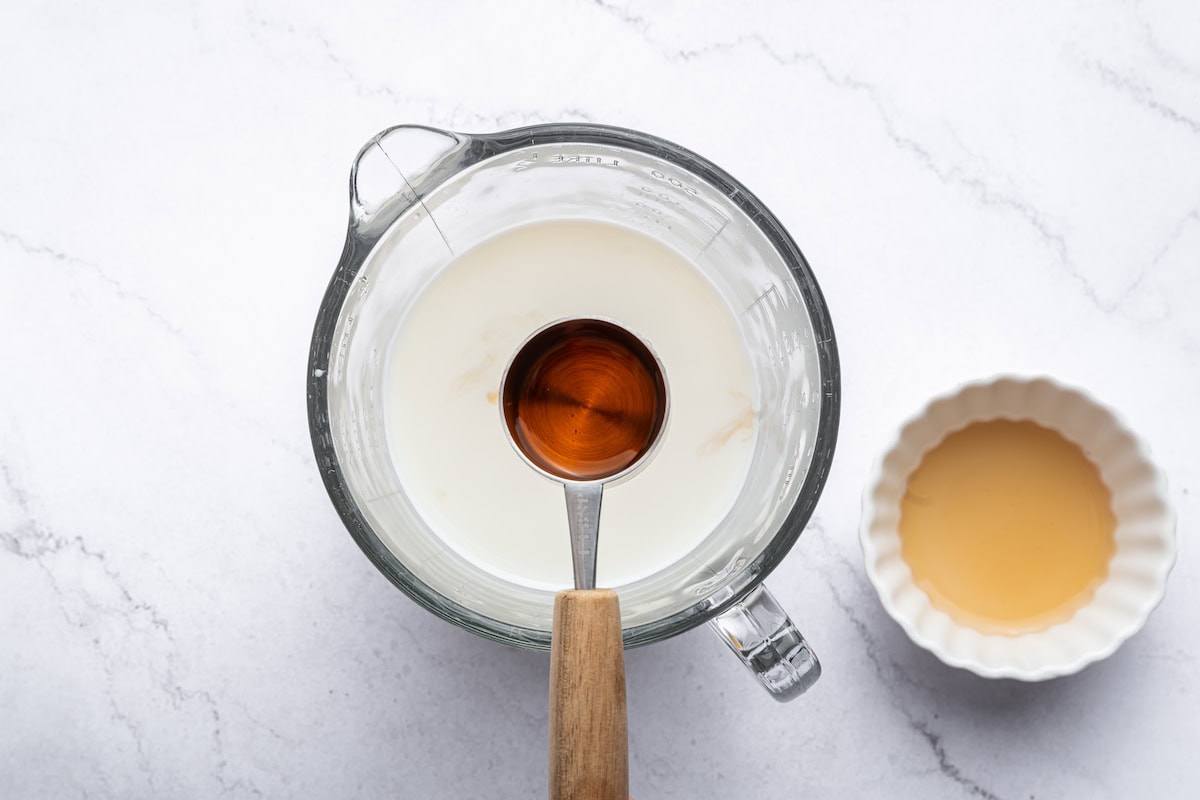 A teaspoon of vanilla extract held over a cup of milk.
