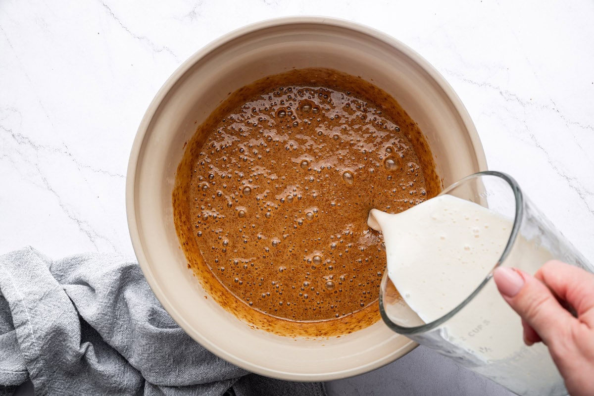Milk is being poured into a large mixing bowl of a chocolate batter used to make a cake.