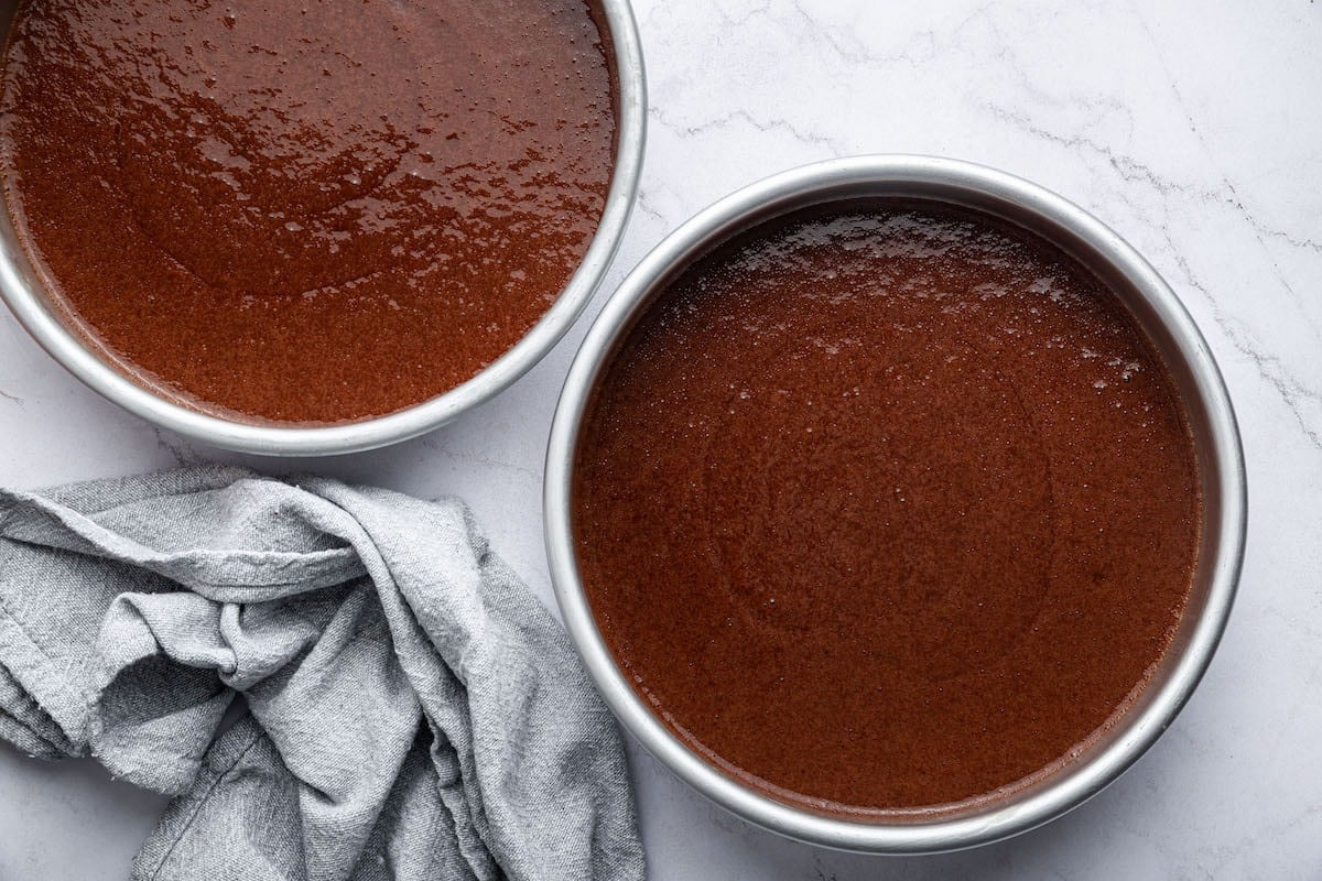 Two circular cake pans with chocolate cake batter.