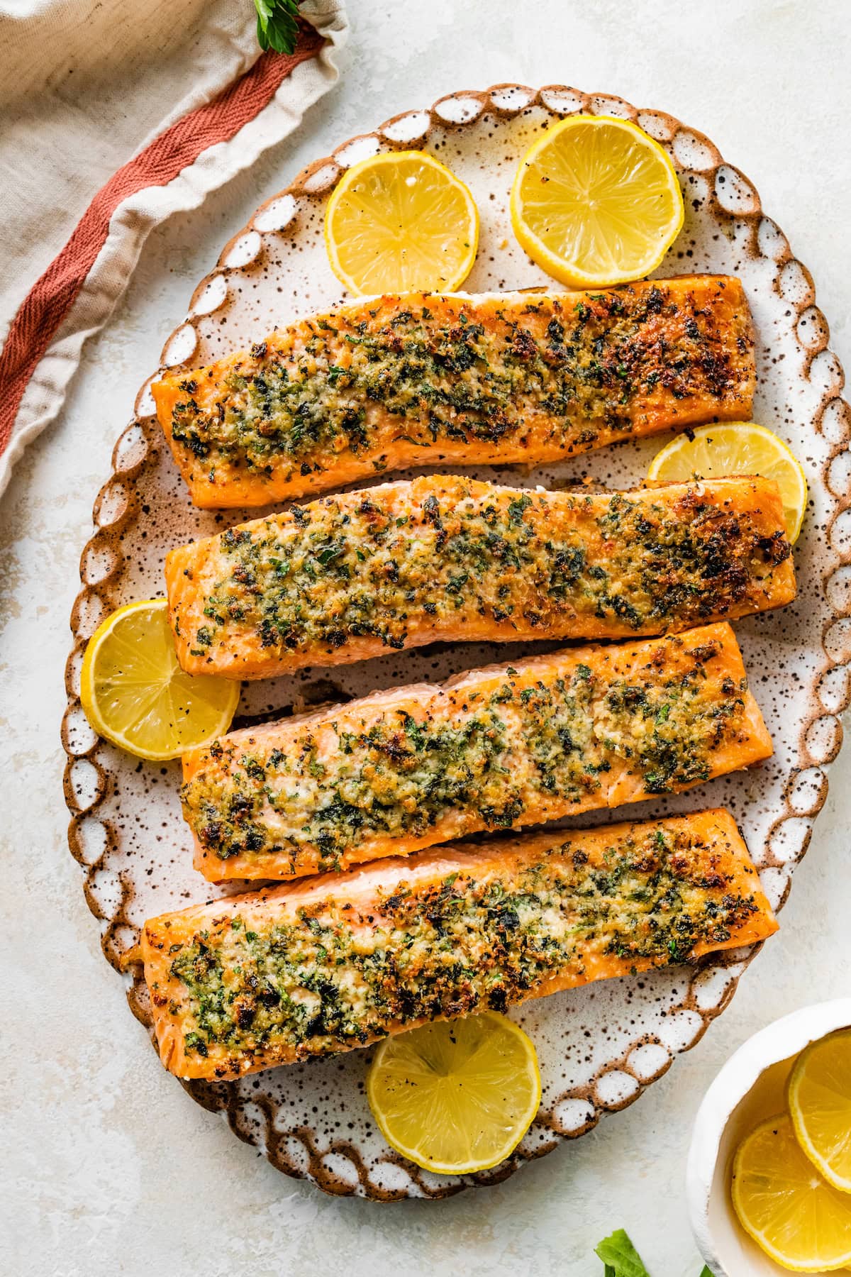 Four parmesan crusted salmon filets served on a speckled tray with multiple lemon slices.