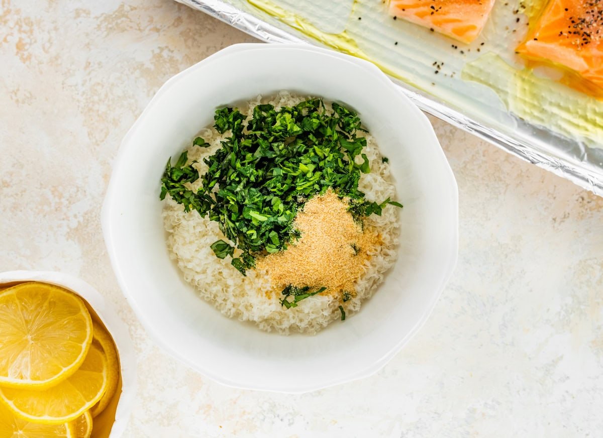 A parmesan herb mixture combined in a small white bowl: parmesan, garlic powder and fresh herbs.